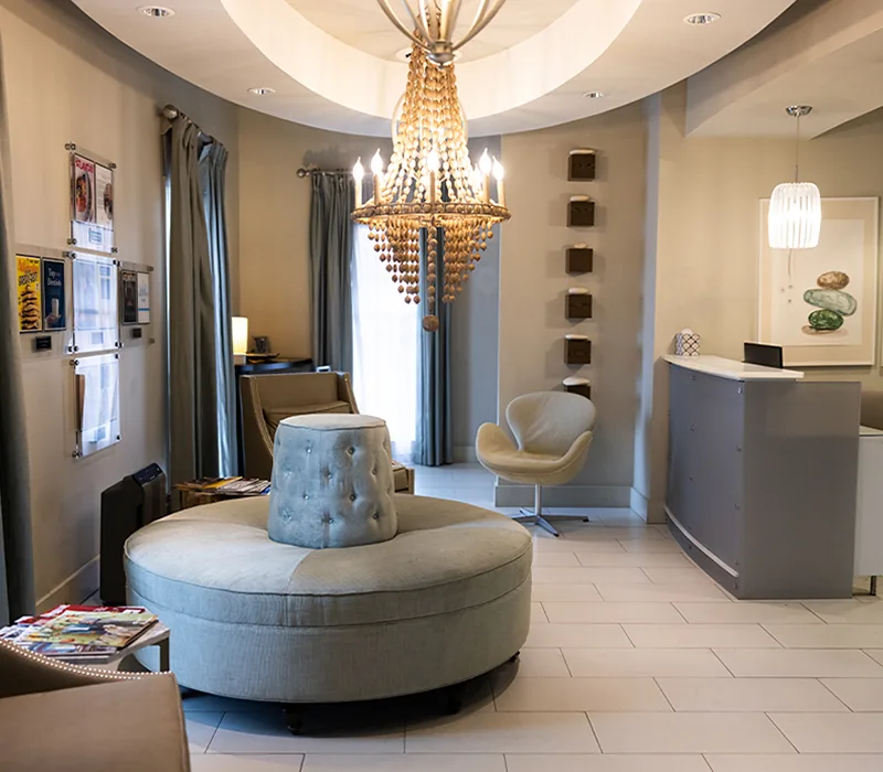 Reception lounge at Signature Smiles Studio, with a round upholstered ottoman beneath a beaded chandelier