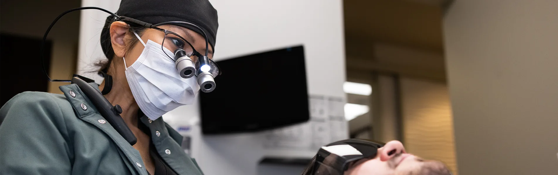 Clinician wearing surgical loupes working over a reclined patient